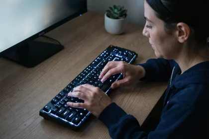 Femme tapant sur un clavier QWERTY rétroéclairé blanc-bleu dans un bureau à domicile sombre la nuit