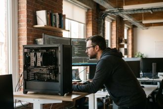 Développeur informatique travaillant sur un PC de bureau avec processeur i5 visible dans un boîtier ouvert, bureau moderne avec plusieurs écrans affichant des benchmarks de performance