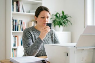 Femme examinant une cartouche d'encre devant une imprimante à la maison dans un bureau domestique
